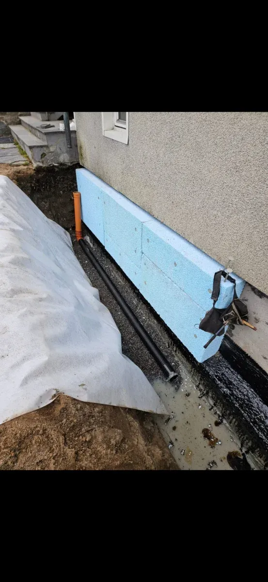 Fuktisolering med blå isolerskivor och svarta dräneringsrör längs husgrund